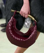 Noémie maroon woven vegan leather handbag with gold-tone hardware held in hand