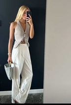 Woman in a beige top and white trousers holding Noémie woven vegan leather handbag with gold-tone hardware