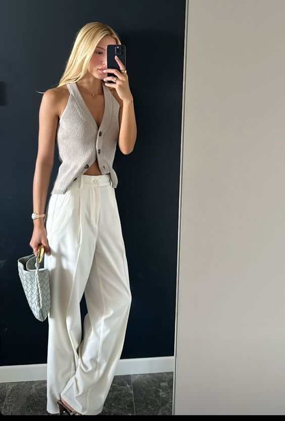 Woman in a beige top and white trousers holding Noémie woven vegan leather handbag with gold-tone hardware
