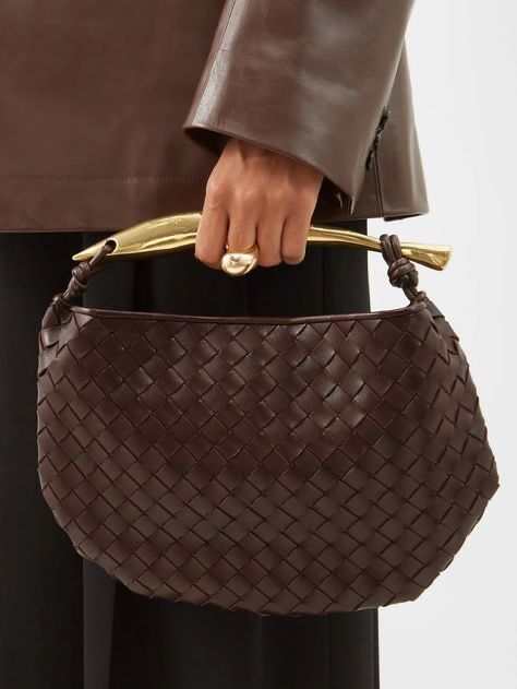 Person in a brown leather jacket holding Noémie brown woven vegan leather handbag with gold-tone handle
