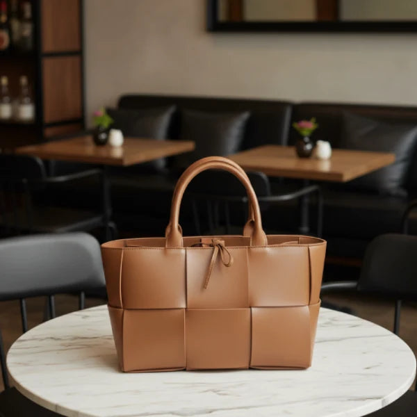 Model carrying Aurelia caramel genuine leather tote bag with a stylish woven design, dressed in a chic outfit in a modern indoor setting