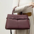 Side view of a woman holding a stylish wine red genuine leather tote bag, featuring elegant buckle detailing and a detachable shoulder strap
