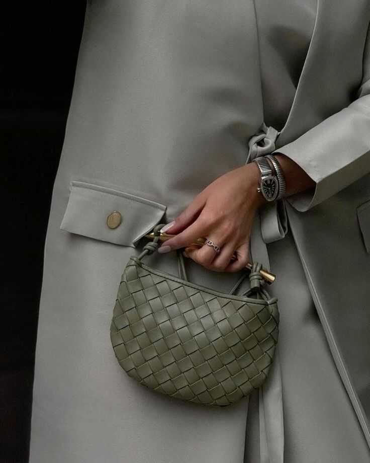 Woman in a grey coat holding Noémie woven vegan leather handbag with gold-tone hardware