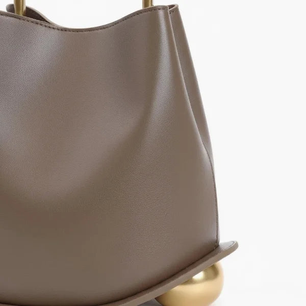 Close-up of a Taupe Izelia top grain leather crossbody bag with gold accents on a white background
