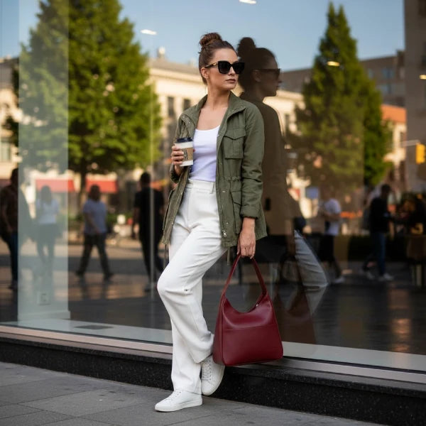 Model holding Seliora vegan leather shoulder bag in wine red while standing on a city street with casual attire