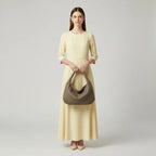 Model standing with grey woven vegan leather hobo bag, wearing a yellow dress, showcasing the bag's elegant design