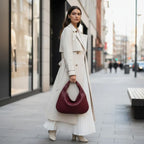 Model standing in an urban setting with a wine red woven vegan leather hobo bag, wearing a beige trench coat